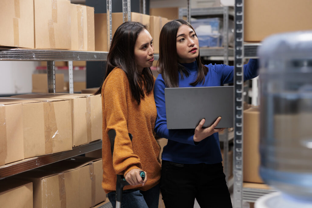 Warehouse managers preparing order, checking pick ticket on laptop